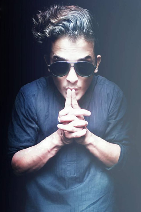 Nouman Rizwan Khan hushing at camera. He is wearing black glasses and black kurta
