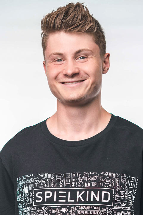 Felix Von Der Laden in short brown hair and blue eyes. He is smiling and wearing a black tee with Spielkind written on it